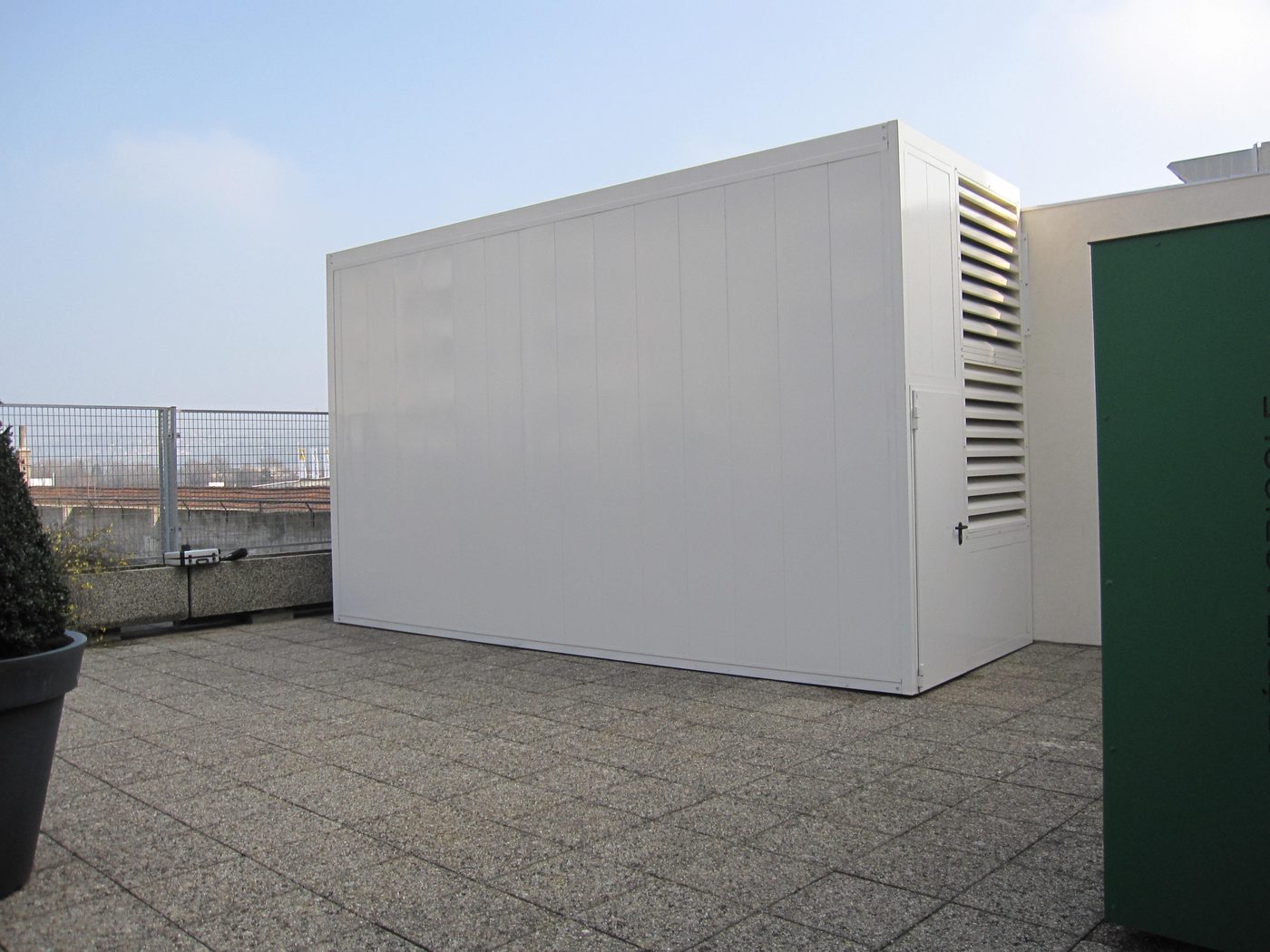 Capotage acoustique d'une pompe à chaleur collective installé en toiture-terrasse, avec grilles de prise et rejet d'air insonorisées